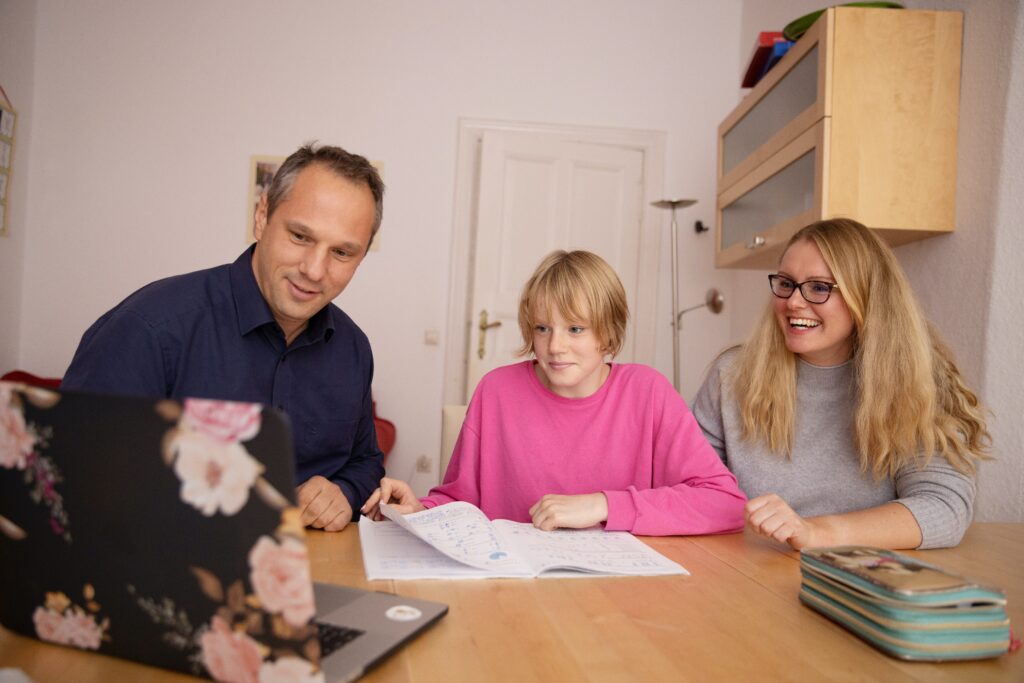 Student in a pink shirt sitting in front of their computer with their two guardians.