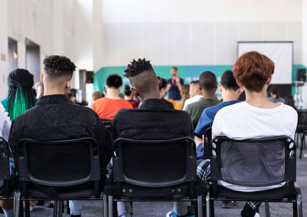 Three students sitting on chairs in the back of a classroom.